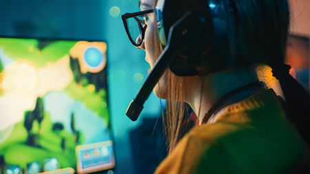 Excited gamer girl in a headset playing on her computer.