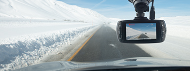 Rejestrator samochodowy zamontowany przy przedniej szybie samochodu jadącego po pustej drodze przez zaśnieżony krajobraz