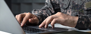 A soldier in camouflage uniform working on a laptop