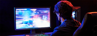 Um gamer em sua mesa com jogo desfocado em seu monitor