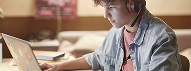 A teenage boy wearing a headset at his desk using a laptop