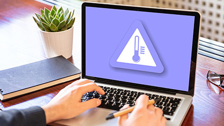 A professional uses a laptop on a desk. The laptop shows a warning sign with a bulb thermometer, indicating an overheating problem.