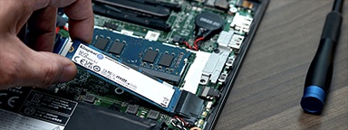 ノート PC に Kingston NV2 SSD を取り付ける手のクローズアップ。