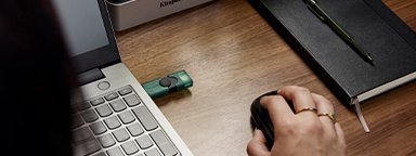 Вид через плечо на USB-накопитель DT Duo, подключенный к ноутбуку, рядом рука использует компьютерную мышь