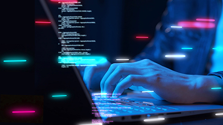 A figure in a leather jacket sits and works on a laptop in the dark, illuminated by monitor light. Bars of bright neon light and lines of code are superimposed on the image.