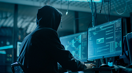 ハッカーを演じるフーディーを着た男がコンピュータを操作しているところ