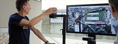 Immagine di 2 tecnici in un ufficio che ispezionano una scheda madre con una lente di ingrandimento su un monitor, con una memoria Kingston installata