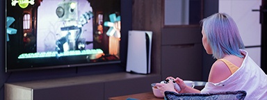 Дівчина-геймерка тримає в руках пульт від PS5, на фоні – відеоекран