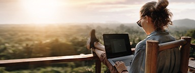 una niña trabajando en una computadora portátil en la puesta de sol en el balcón