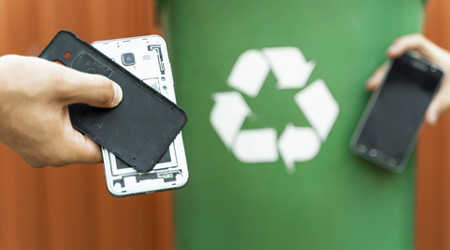 リサイクル用ごみ箱を背景に、携帯電話のパーツを持つ手