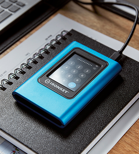 On a work desk, a Kingston IronKey Vault Privacy 80 External SSD is connected to a laptop. Its touchscreen keypad is visible. A perfect tool for securing data while traveling or working remote.