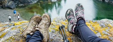 Os pés de duas pessoas pendurados sobre a beira de uma rocha com vista para um lago.