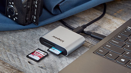 一张放有各种摄像设备的桌子，一台带无线鼠标和键盘的笔记本电脑，以及多张 Kingston SD 卡和 microSD 卡。