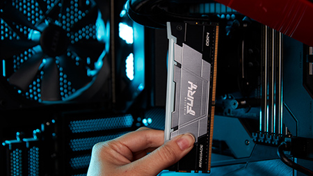 Một bàn tay cầm thanh RAM Kingston FURY Renegade DDR4 RGB bên trong một thùng máy đỏ đen sành điệu.