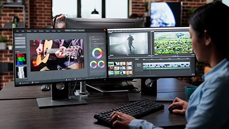 Hombre sentado en un escritorio utilizando un ratón para editar vídeo en un portátil con un segundo monitor grande.