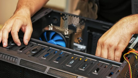 A man with his hands in an open PC tower case, cables spilling out over its side.