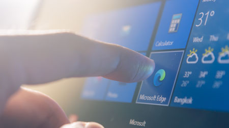 一个手指按下平板电脑触摸屏上 Microsoft Edge 的图标。该平板电脑运行的是 Windows。