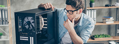 Mężczyzna siedzący przy biurku z otwartą obudową komputera i przyglądający się komponentom znajdującym się wewnątrz i na zewnątrz.