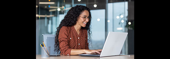 A smiling woman works on a laptop at a desk
