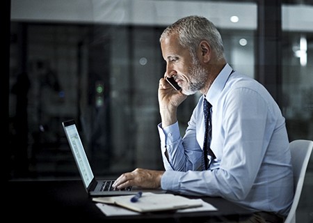 um homem usando o laptop e telefone no trabalho no escritório à noite