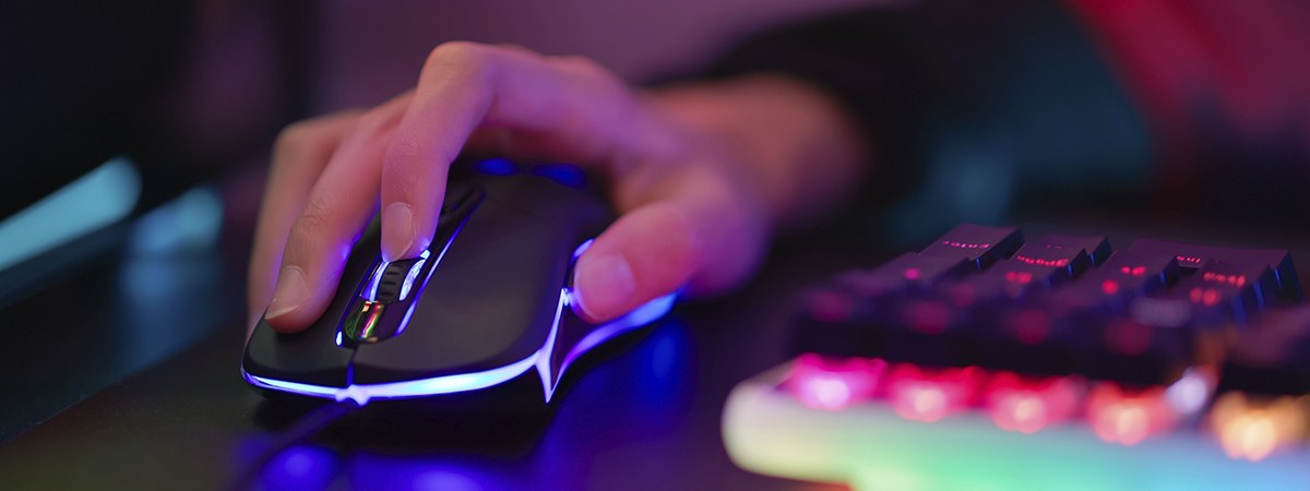 Una mano desplaza la rueda de un rat&oacute;n RGB, con un teclado RGB desenfocado en primer plano