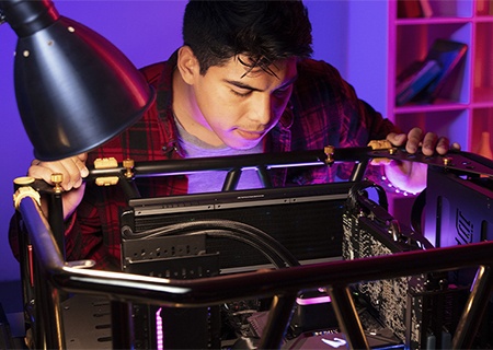 ein junger Mann, der in sein offenes Desktop-Computergehäuse auf einem Schreibtisch schaut, um einen neuen Gaming-PC zu bauen