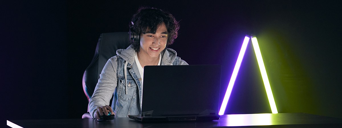 Ein Gamer spielt an seinem Laptop in einem dunklen Raum mit Neonlicht im Hintergrund