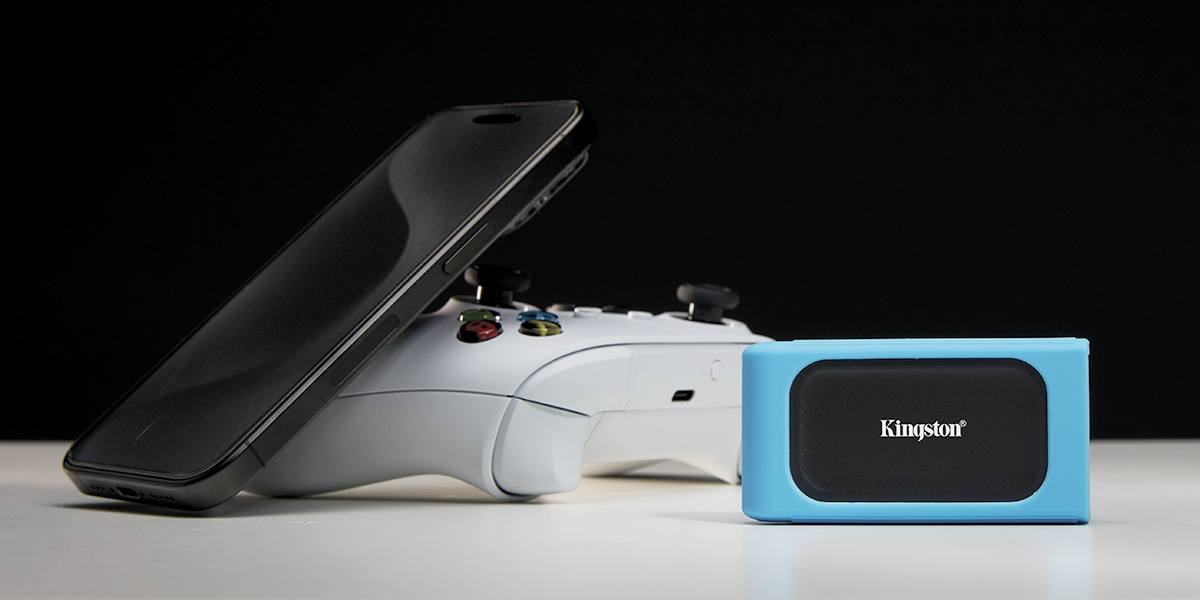 Un drive SSD XS1000 su un tavolo accanto a un iPhone 15 e a un controller Xbox