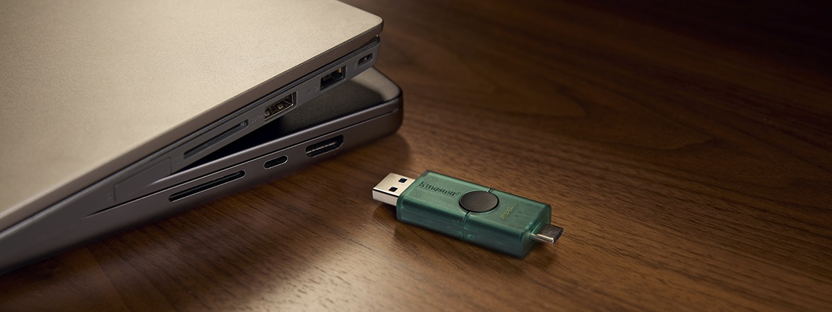 USB DT Duo con cappucci fatti scorrere indietro per mostrare i connettori, posizionato vicino a laptop Windows e Mac
