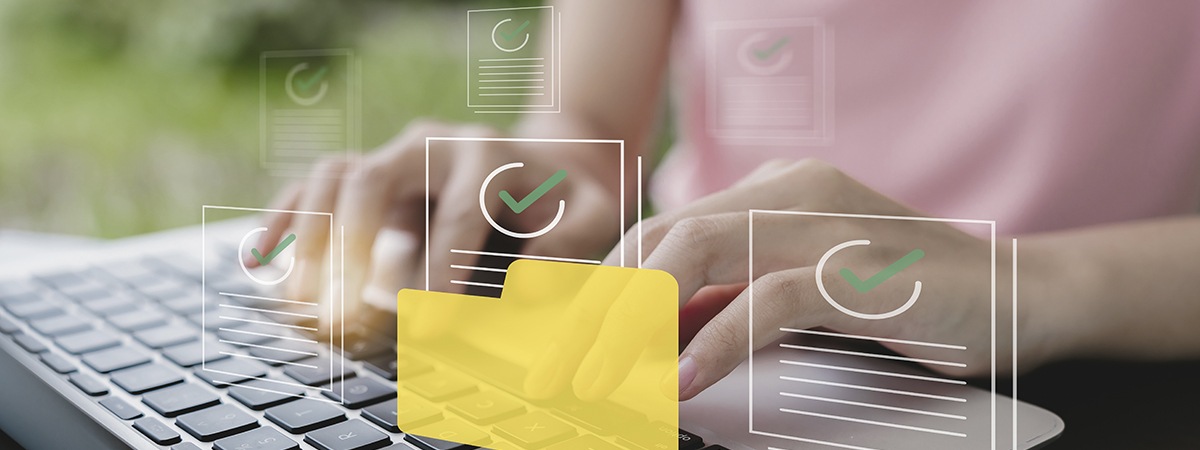 Icone di file con segno di spunta verde; sullo sfondo, sfocata, una persona che fa il backup dei dati su un laptop