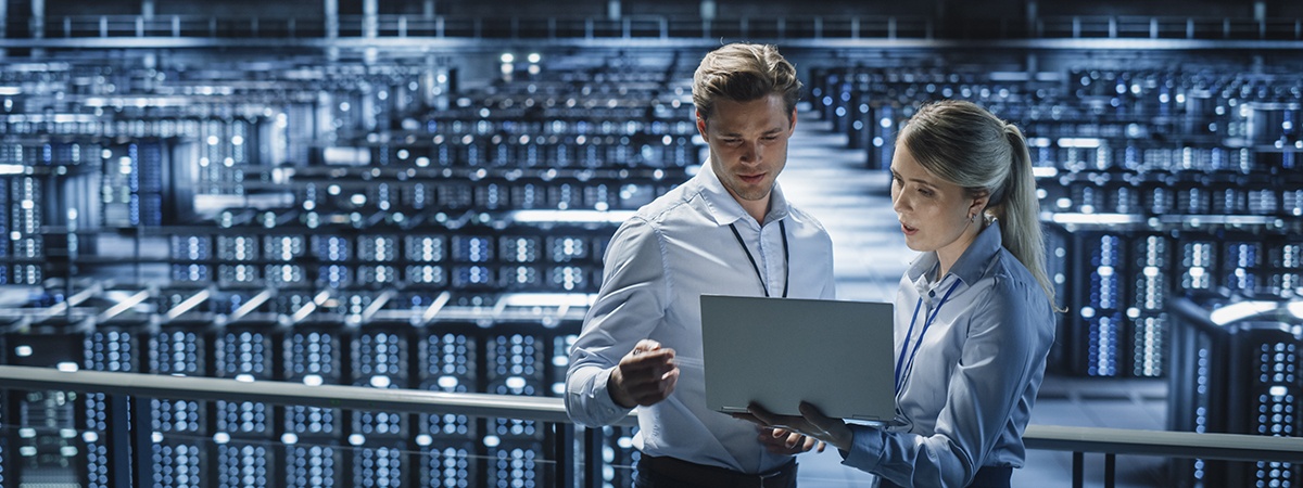 Manager aziendale ed esperto IT discutono dell'infrastruttura server tenendo in mano un laptop su un ponte sopra un data center moderno