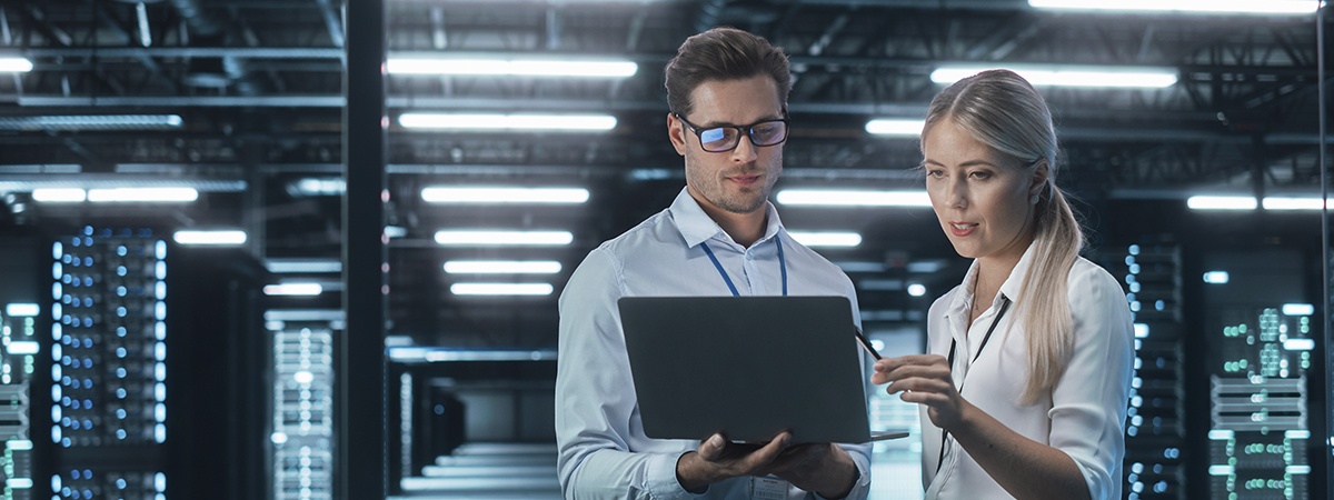 Ingenieur und IT-Manager besprechen ein Upgrade an einem Laptop in einem Rechenzentrum, im Hintergrund Serverg&auml;nge