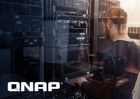 інженер, який працює на своєму ноутбуку в серверній кімнаті з логотипом QNAP на передньому плані