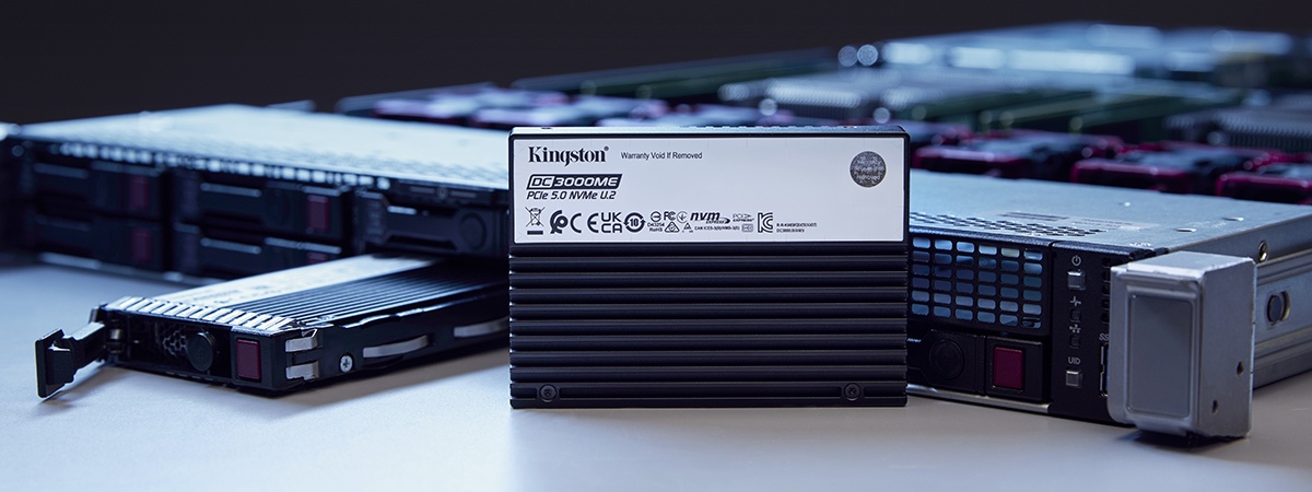 Two Kingston DC3000ME SSDs, one standing, the other flat in front of a server rack on the table