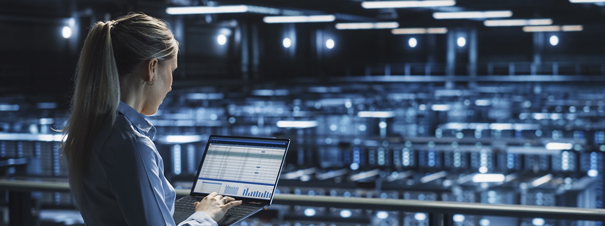 An engineer using her laptop, overlooking a large server farm