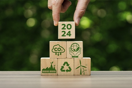 A hand placing a 2024 wooden block on sustainability ones