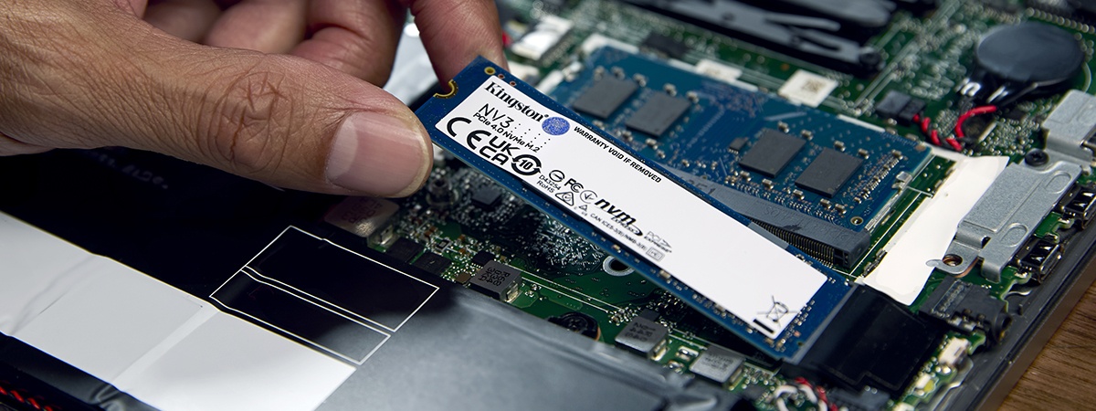 Рука крупным планом, устанавливающая твердотельный накопитель Kingston NV3 NVMe в ноутбук с установленным модулем памяти Kingston
