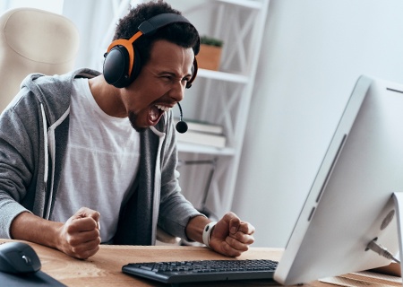 Młody mężczyzna siedzi w domu przy biurku, krzycząc na swój komputer