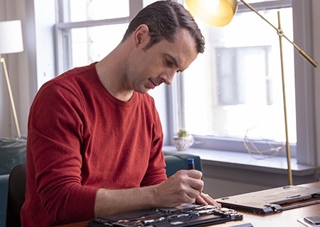 Mężczyzna siedzący w domu przy biurku i modernizujący podzespoły swojego laptopa