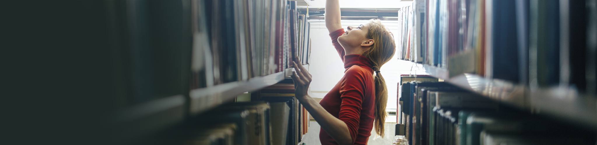 A young librarian searching books and taking one book from library bookshelf