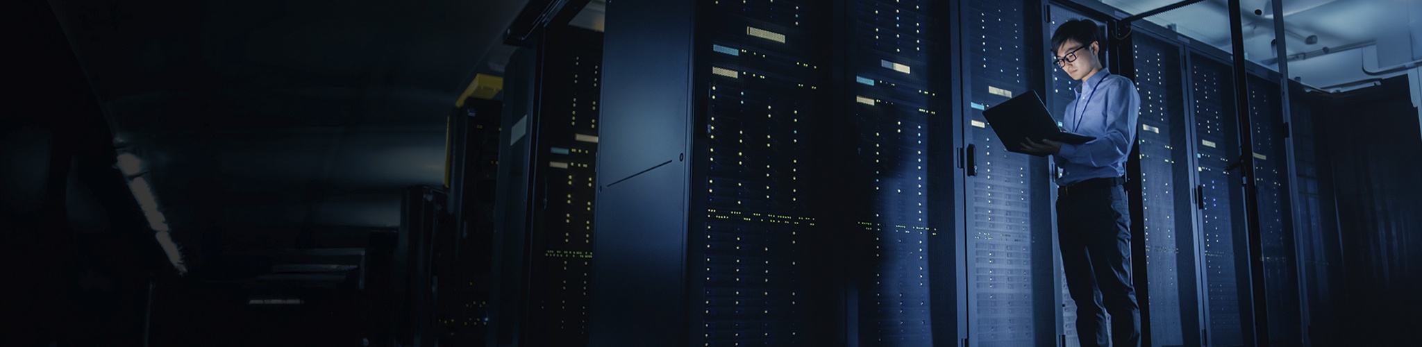 An IT worker in a dimly lit server room standing while using a laptop PC