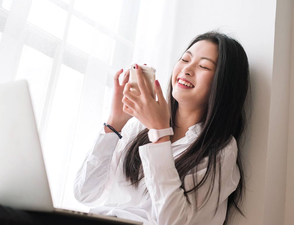 Một người phụ nữ đang mỉm cười trong khi sử dụng điện thoại thông minh