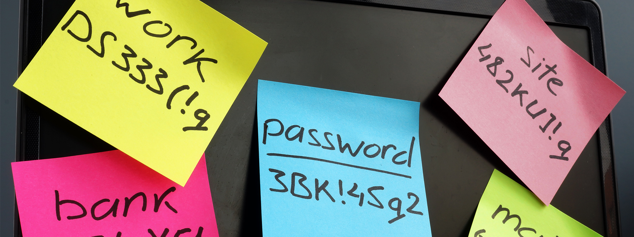 Gestione password. Laptop con note indicanti password complesse sullo schermo.