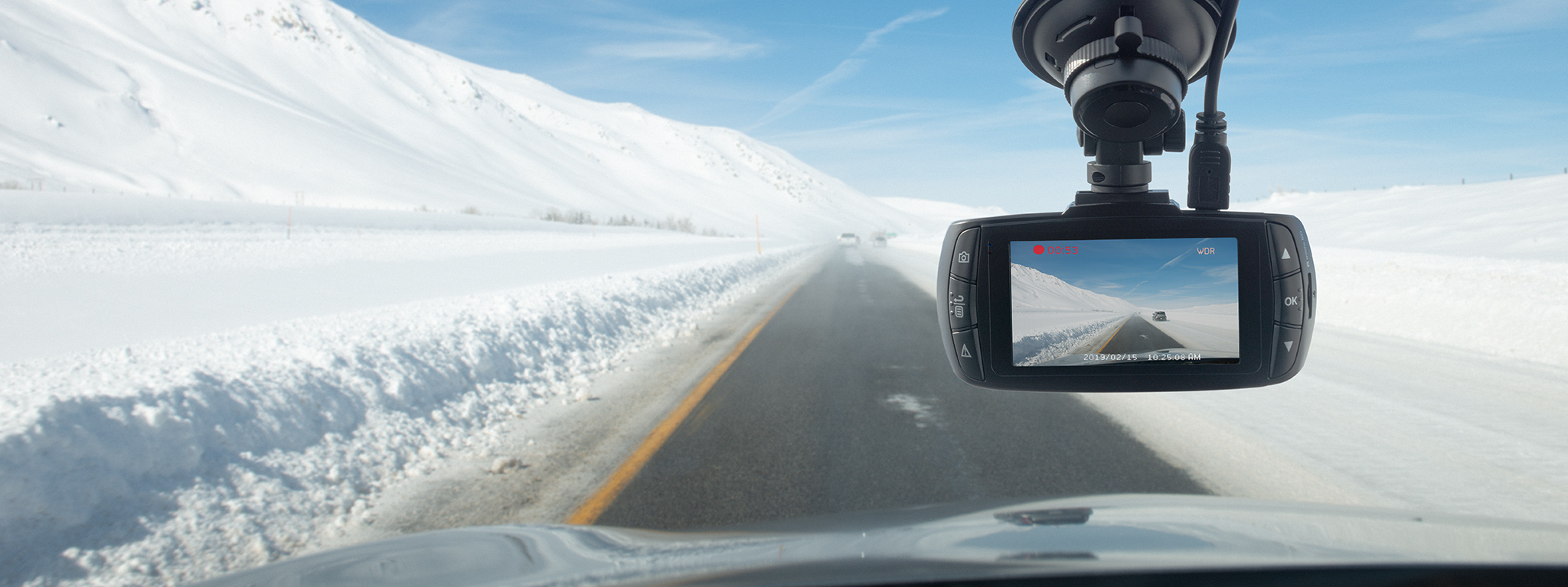 Dashcam montada detrás de un parabrisas en una carretera despejada con un paisaje cubierto de nieve