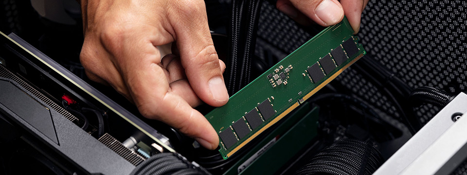 Qu’est-ce que l’AEMP ? Mains tenant un module de mémoire DDR5 Kingston ValueRAM à l’intérieur d’une carte mère, sur le point d’installer le module