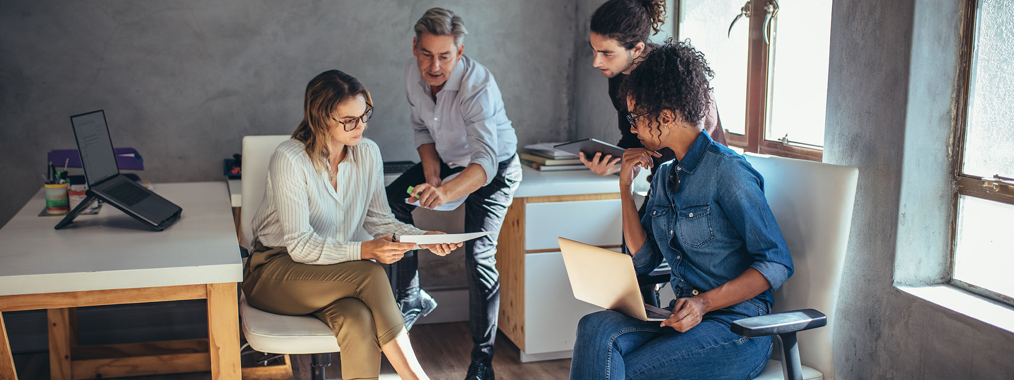 Four office workers collaborate using various devices.