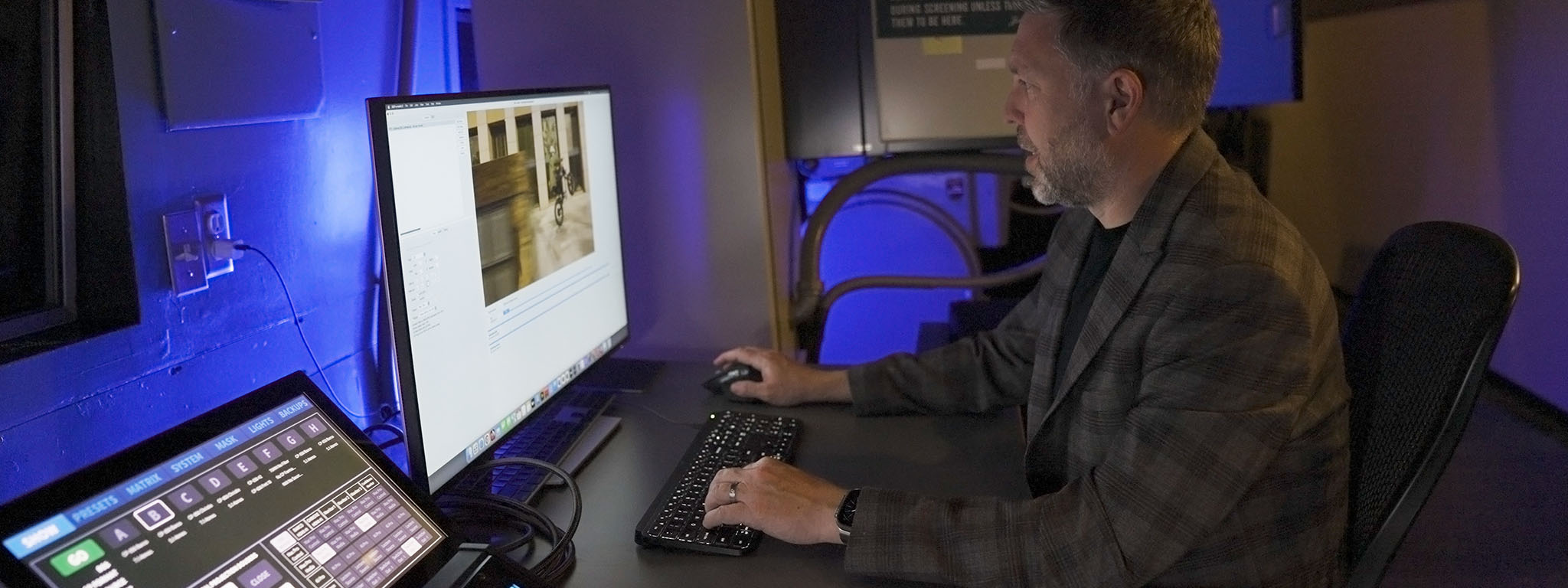 Dijital Projeksiyoncu Ryan Carpenter bir bilgisayar monitörünün başında oturuyor.