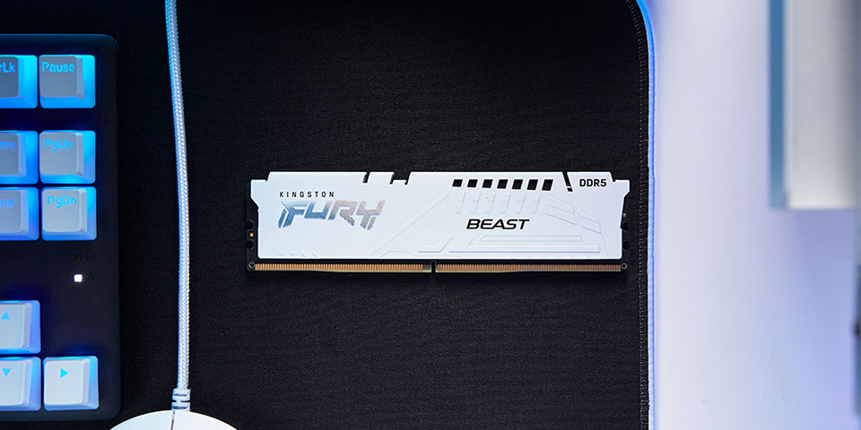 Un m&oacute;dulo de memoria Kingston FURY blanco sobre un escritorio junto a un rat&oacute;n y un teclado.