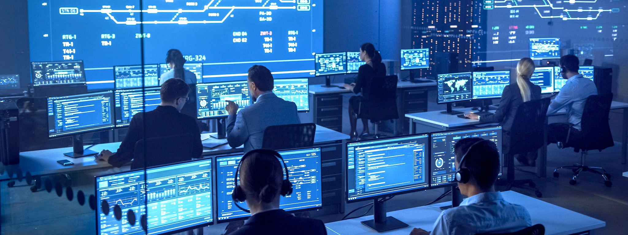 Immagine di un team di sicurezza nazionale in una sala di monitoraggio davanti a schermi di PC raffiguranti tabelle, grafici e statistiche