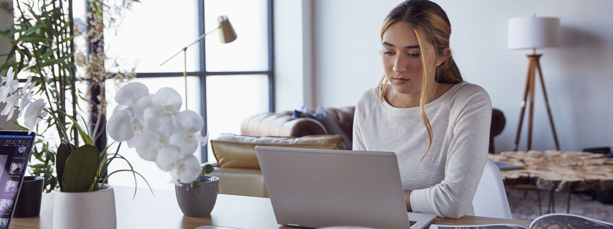 Une fille à la maison, assise à une table et travaillant sur son ordinateur portable